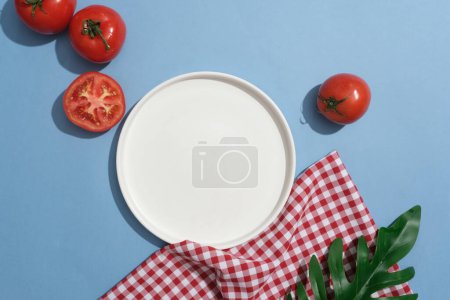 Photo for A red and white checkered fabric and green leaf displayed with empty dish and tomatoes. One of the benefits of tomato for skin is that it helps repair damaged skin - Royalty Free Image