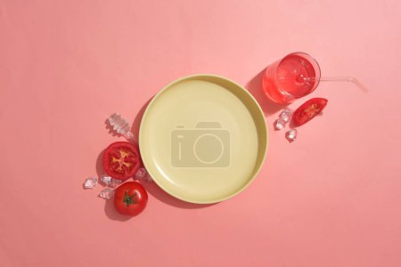 Téléchargez les photos : Un plat rond de couleur jaune avec quelques tranches de tomate, des tranches et un verre de jus de tomate. Espace vide sur le plat pour montrer le produit cosmétique de l'extrait de tomate - en image libre de droit
