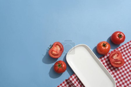 Téléchargez les photos : Un plat en céramique disposé avec des tomates rouges sur fond bleu. Les tomates sont une excellente source naturellement disponible et peu coûteuse de fruits riches en antioxydants. - en image libre de droit