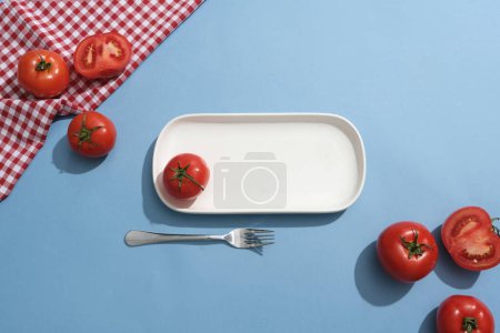Foto de Algunos tomates decorados con un plato blanco vacío y un tenedor. Los tomates mantienen la piel bien hidratada y suprimen la producción de aceite de la piel - Imagen libre de derechos