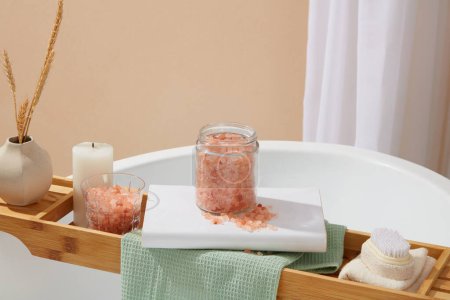 Foto de Concepto de baño con un frasco de sal rosa himalaya arreglado con otros suministros en la bandeja de la bañera de madera. Algunos afirman que la sal del Himalaya es más natural que la sal de mesa - Imagen libre de derechos