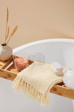 Téléchargez les photos : Le concept de cosmétique naturelle avec baignoire comportait une éponge de bain, une brosse à pieds et une tasse en verre de sel d'himalaya rose. Espace vide sur l'écharpe beige pour afficher votre produit - en image libre de droit