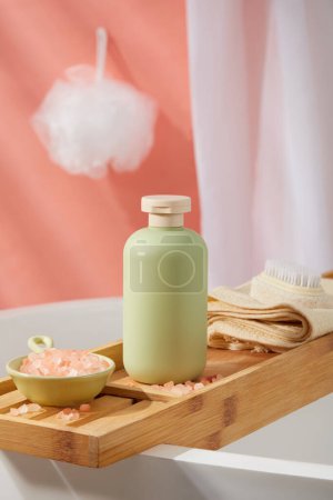 Photo for A bottle in pastel color placed on a bathtub tray with a dish containing pink himalayan salt and a towel with foot brush. White bath sponge hanging on the wall. Empty label for branding mockup - Royalty Free Image
