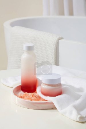 Photo for Rounded marble tray with a blank label bottle and jar placed on. A handful of pink himalayan salt displayed. Background with a bathtub with white towel hanging on. Branding mockup - Royalty Free Image