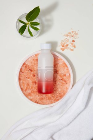 Photo for White towel placed next to a round tray of pink himalayan salt and blank label bottle. Branding mockup design. Himalayan salt can loosen away any dandruff on your scalp - Royalty Free Image
