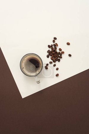 Foto de Sobre el fondo de papel blanco y marrón, una deliciosa taza de café decorada con granos de café tostados marrones. Fondo creativo para la publicidad. El café tostado es un tónico para el pensamiento y la creatividad - Imagen libre de derechos