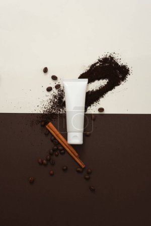 Téléchargez les photos : Fond blanc et brun créatif pour la publicité cosmétique avec ingrédient de café. Un tube en plastique blanc avec grains de café, poudre de café et bâton de cannelle décoré - en image libre de droit