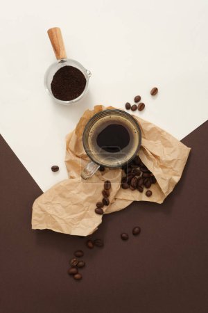 Photo for A glass coffee cup decorated with coffee beans on paper and coffee powder on a glass tray on a colored background. Minimalist scene to advertise traditional drinks - Royalty Free Image