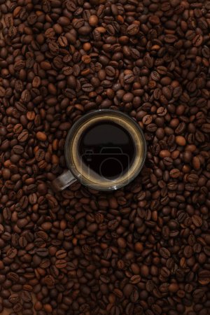 Photo for Top view of glass cup of coffee espresso displayed on brown roasted coffee beans background. Minimal scene for advertising. Active caffeine in coffee makes you awake, refreshed and work more focused - Royalty Free Image