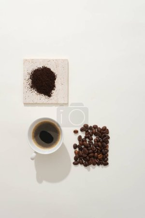 Téléchargez les photos : Café en grains et poudre de café sur le podium en brique décoré d'une délicieuse tasse d'espresso sur fond blanc. Concept minimaliste pour la publicité, ingrédients naturels pour une boisson rafraîchissante - en image libre de droit
