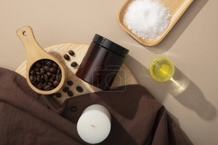 Photo for On the beige background, an amber jar without label decorated with coffee beans and bath salt in wooden trays, dark brown cloth and candle. Mockup scene for design, advertising product for body care - Royalty Free Image