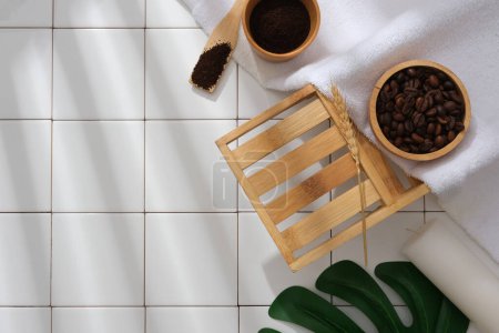 Photo for White tiles background for advertising organic product with bathroom concept. Coffee beans and coffee powder on wooden bowls with white towel and green leaf decorated. - Royalty Free Image