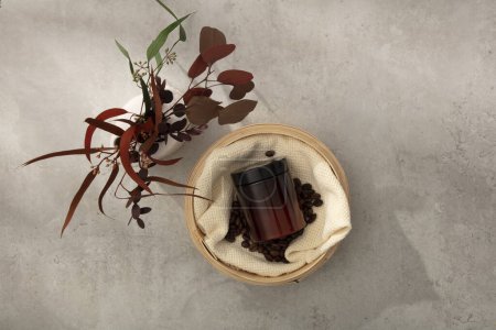 Photo for Top view of an amber cosmetic jar unlabeled placed on bamboo basket with coffee beans and beige cloth. Beside is a vase with dry branch leaves on cement floor. Minimal scene for advertising - Royalty Free Image