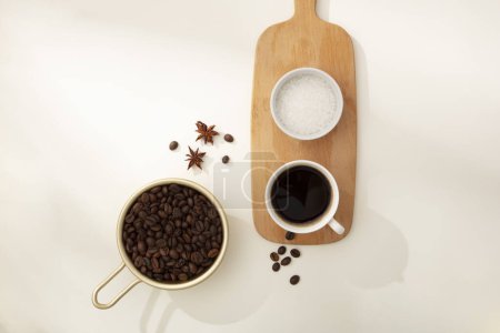 Photo for Against the white background, coffee beans on golden tray decorated with cup of coffee and bowl of bath salt on wooden cutting board. Natural ingredients for body skin care - Royalty Free Image