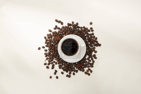Téléchargez les photos : Vue de dessus de tasse de café en céramique placée sur des grains de café torréfiés bruns sur fond blanc. Café propre est un ingrédient actif efficace qui aide à réduire la dépression du système nerveux - en image libre de droit