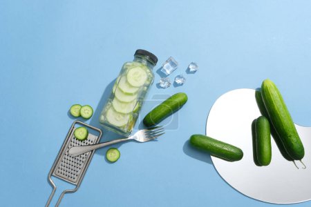 Photo for Several cucumbers arranged with a detox water bottle, ice cubes, a grater and a fork. Cucumber (Cucumis sativus) can control the oil production of your skin - Royalty Free Image