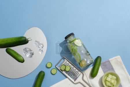 Photo for A mirror with small cucumbers and ices placed on. Unbranded bottle without label of detox water displayed with a grater. Cucumber is antioxidant-rich - Royalty Free Image