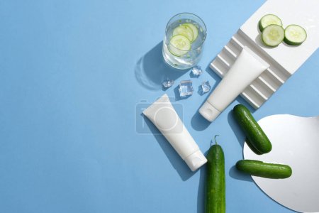 Photo for Two white tubes decorated with a staircase, ices and a mirror. A glass of cucumber detox water is featured. Skin care concept with empty label for Cucumber extracted product - Royalty Free Image