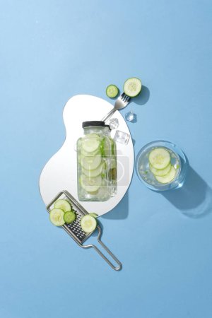 Photo for Top view of unbranded water bottle placed on a mirror. A glass filled with cucumber detox water displayed. Cucumber (Cucumis sativus) is one of the natural ingredients - Royalty Free Image