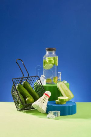 Foto de Botella de agua de desintoxicación de pepino de pie en un podio, que se muestra con un trasbordador y una cesta de pepinos frescos. Concepto de fruta orgánica saludable - Imagen libre de derechos