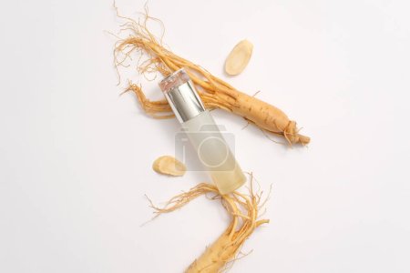 Vue du dessus de la bouteille vide affichée avec des racines de ginseng frais sur fond blanc. Le ginseng est un ingrédient largement utilisé dans les cosmétiques avec de nombreux avantages pour la peau. Photo publicitaire