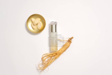 Photo for Top view of empty cosmetic bottle decorated with fresh ginseng roots and dish of ginseng slices on white background. Mockup for advertising ginseng root extract cosmetics. Flat lay. - Royalty Free Image