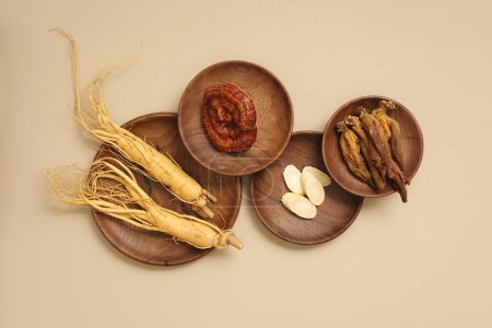 Photo for Top view of rare herbal displayed on wooden dishes - ginseng roots, ganoderma mushrooms and red ginseng. Beige background for advertising product and space for design - Royalty Free Image