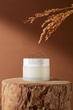 Photo for Close-up of a jar of unbranded lotion placed on a log on a brown background. Vitamin B1 in rice bran is a savior in skin care, repelling the process of melanin formation. - Royalty Free Image