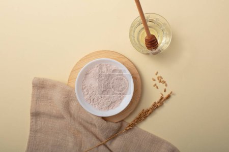 Photo for Rice bran powder is displayed on a ceramic plate on a wooden platform. A honey drizzle is placed in a glass of water. Rice bran powder is very effective in tightening pores and removing dirt. - Royalty Free Image