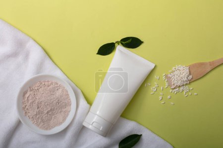Photo for Rice bran powder on a ceramic plate, a white tube without label, white fabric and green leaves on a pastel background. Skin care concept with natural ingredients. - Royalty Free Image