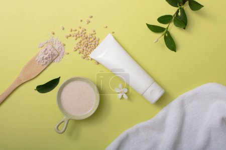 Photo for Rice bran powder rests on a ceramic plate, accompanied by an unlabeled white tube, soft fabric and green leaves on a soothing pastel backdrop. Embracing natural ingredients in skincare. - Royalty Free Image