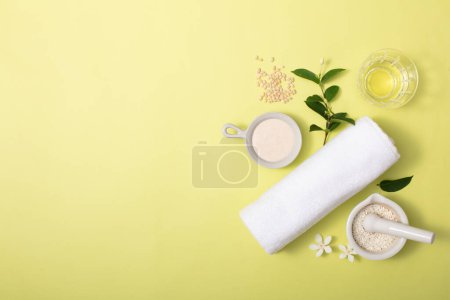 Photo for Rice bran powder is contained in ceramic utensils, green leaves, a glass and a towel on a light yellow background. Free space for design or product display. Skin care with rice bran. - Royalty Free Image