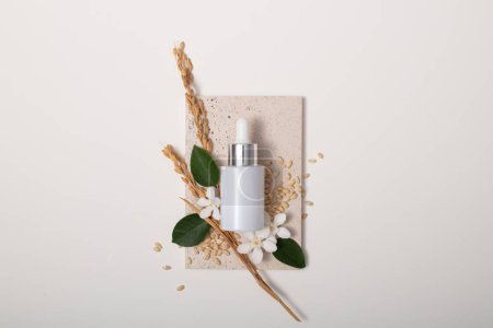 Photo for A white serum jar is displayed on a podium with whole grain rice, green leaves and camellia flowers. The composition of rice bran contains phytosterols - which have antioxidant effects. - Royalty Free Image