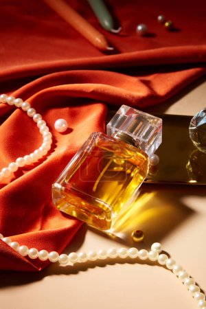 Foto de Una botella de perfume sin etiqueta se muestra en una mesa con una cadena de perlas, velas y seda roja. Burla para la publicidad de perfumes con etiqueta en blanco. - Imagen libre de derechos