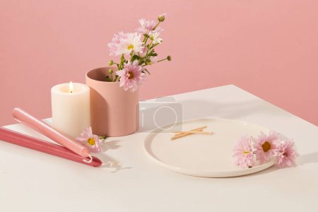 Foto de En la mesa blanca hay velas, flores frescas, una taza de cerámica y un plato de cerámica con un fondo rosa. Espacio para la visualización del producto. Tema de belleza. - Imagen libre de derechos