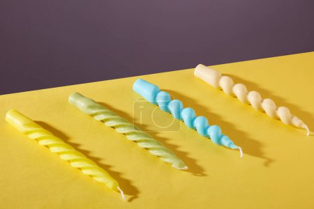 Foto de Cuatro velas retorcidas en cuatro colores: amarillo, verde pastel, azul y beige sobre un fondo amarillo púrpura. La luz de las velas aporta calidez, pasión e inspiración. - Imagen libre de derechos