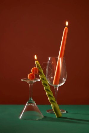 Téléchargez les photos : Deux bougies allumées sont placées à côté d'un verre à cocktail et d'un verre à vin sur un fond vert foncé et brun. Espace mystérieux pour la publicité et d'autres fins. - en image libre de droit