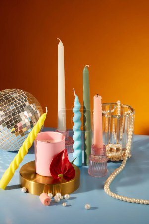 Foto de Velas de colores se muestran en una mesa con una cadena de perlas, un vaso y una bola de discoteca. El colorido espacio es adecuado para cumpleaños y vacaciones. - Imagen libre de derechos