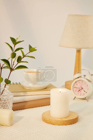 Téléchargez les photos : Bougie est placée sur une plate-forme ronde en bois. Les feuilles vertes sont placées dans un vase en verre. Tasses à café, cahiers, lampe et horloge sont affichés sur un fond minimaliste. Espace de copie. - en image libre de droit