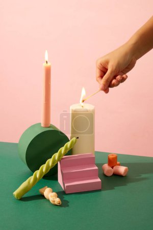 Photo for Close up of man hand lighting candles on pink background. Colorful platforms on deep green table. Candles are commonly used for decoration and lighting. - Royalty Free Image