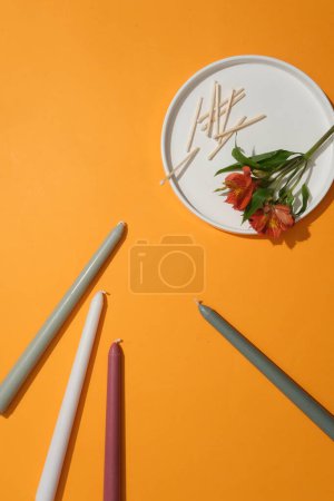Photo for A flower branch and matchsticks are placed on a white ceramic plate. The candles are placed randomly on a yellow background. Candles are used for lighting and decoration. - Royalty Free Image