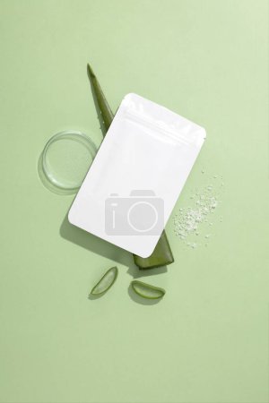 Photo for Close-up of an unbranded mask sheet placed on a fresh aloe vera leaf, next to a transparent petri dish on a pastel background. Mockup for cosmetic brand advertising. - Royalty Free Image