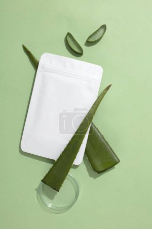 Photo for A non-branded mask sheet rests on a fresh aloe vera leaf, beside a clear petri dish, set against a pastel background-a cosmetic brand mockup. Copy space. - Royalty Free Image