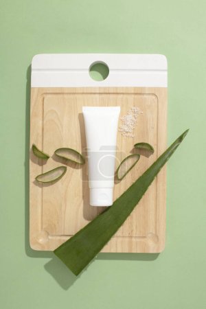 Photo for Top view of an empty plastic tube and fresh aloe vera leaves displayed on a wooden cutting board. Cosmetic concept with natural extracts - safe and benign for the skin. - Royalty Free Image