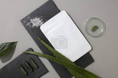 Photo for Close-up of a mask sheet placed on a dark surface with fresh aloe vera leaves. A transparent petri dish is placed next to it. Scene for advertising cosmetics with natural ingredients. - Royalty Free Image