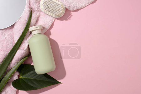 Photo for A towel is spread out in the left corner of the frame with a brush, an unlabeled bottle of shower gel, fresh aloe vera leaves and a mirror on a pink background. Empty space for text design. - Royalty Free Image