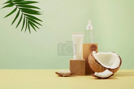 Photo for Pastel background with unlabeled cosmetic bottles placed on wooden podium. Fresh coconut and tropical palm leaves. Mockup for vegan cosmetics advertisement. - Royalty Free Image