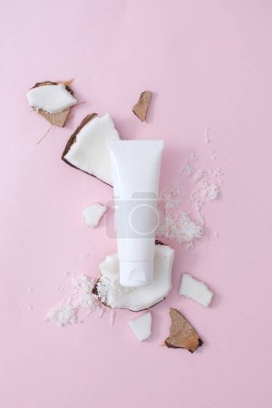 Photo for White plastic cosmetic tube placed on fresh coconut pieces on a pink background. Cosmetic concept of fresh coconut extract. Scene for advertising. - Royalty Free Image