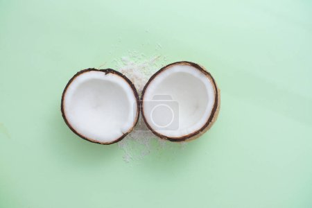 Téléchargez les photos : Les noix de coco fraîches sont coupées en deux et certaines copeaux de noix de coco sont affichés sur un fond minimaliste. Conception de produits cosmétiques. Maquette pour la présentation de produits de beauté. Vue du dessus. - en image libre de droit