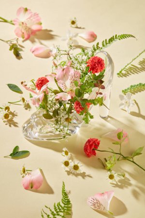 Photo for Pink petals and green leaves are scattered on a beige background. A transparent glass shoe is placed in the center and decorated with flowers and leaves. Creative image. - Royalty Free Image